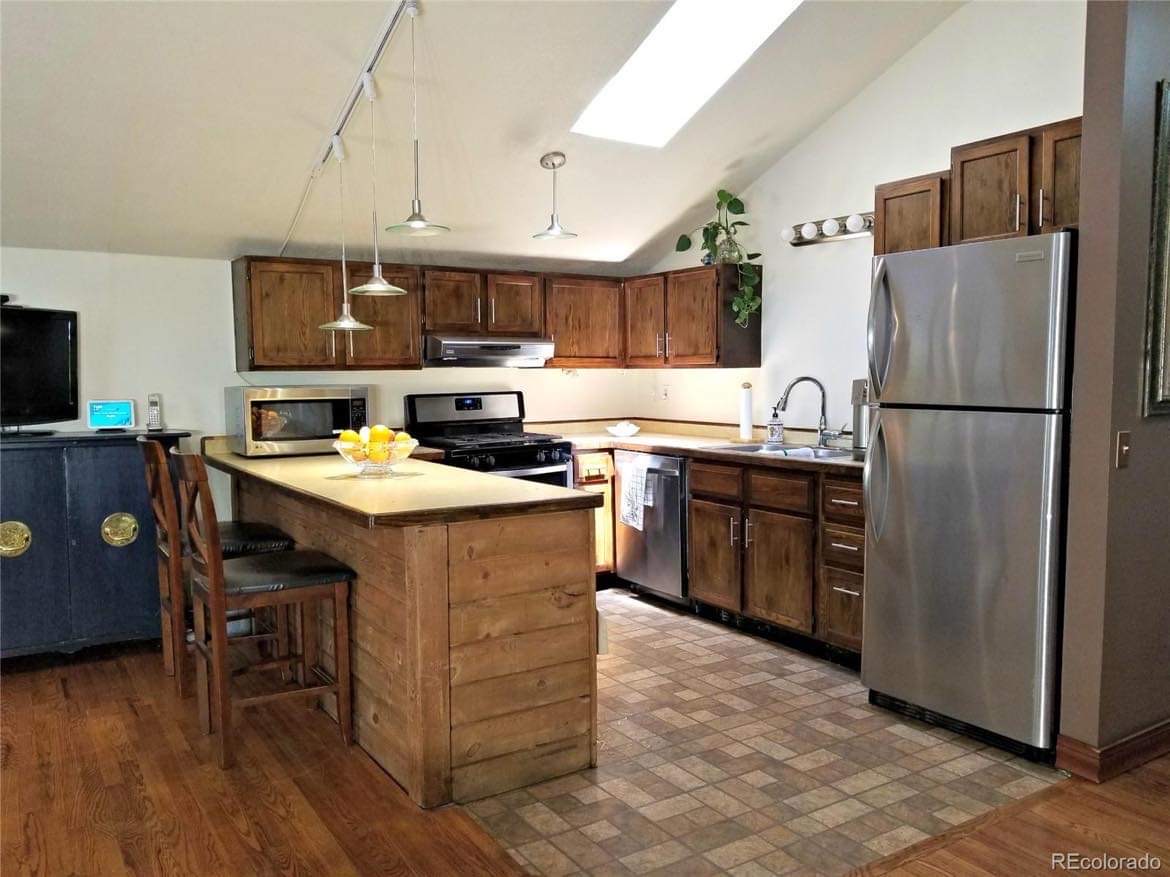 kitchen before the DIIY update with pain, sink, lights, bead board backsplash, cheap flooring, pot rack, painted countertops